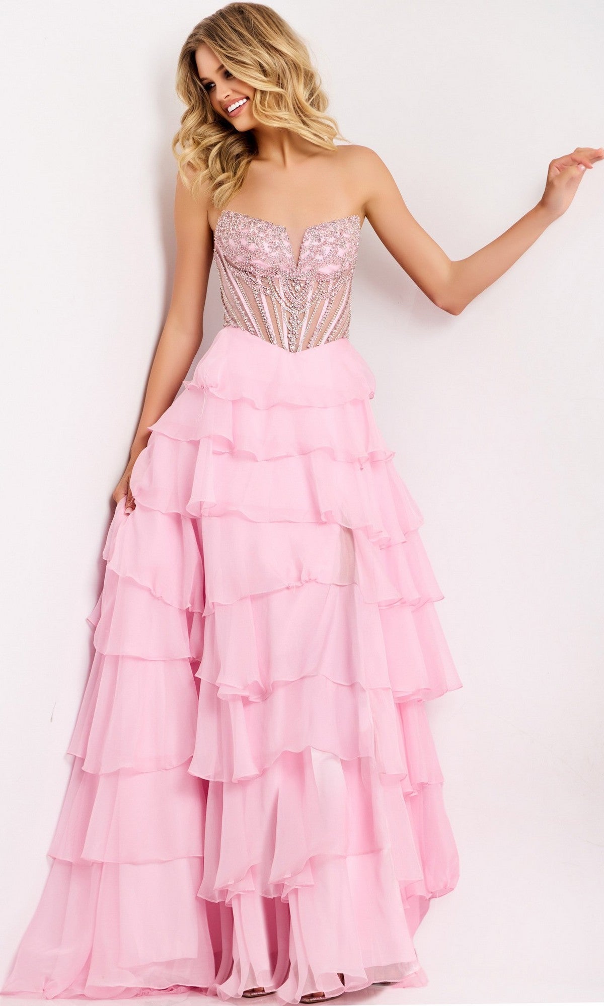 A woman stands against a plain white background wearing the Jovani 49109 long prom dress in light pink, featuring a strapless beaded corset bodice and a layered chiffon skirt.